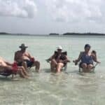 Group of guests sitting together in shallow water at a Key West sandbar